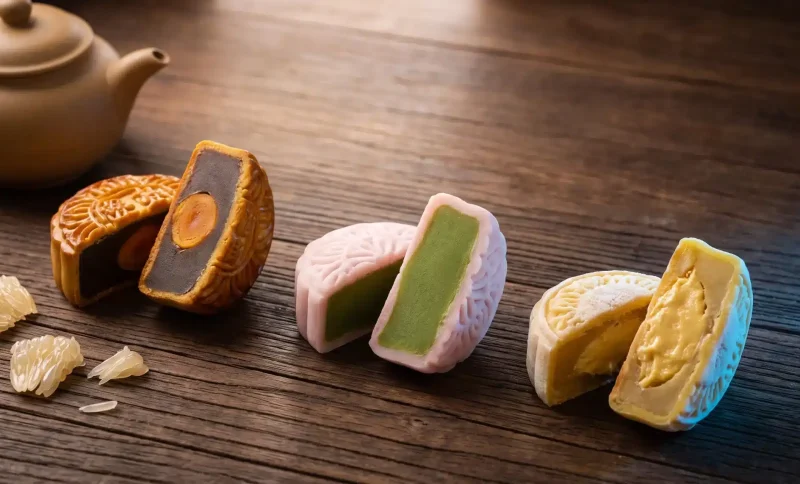 Three mooncakes with different fillings on a wooden table beside a brown teapot