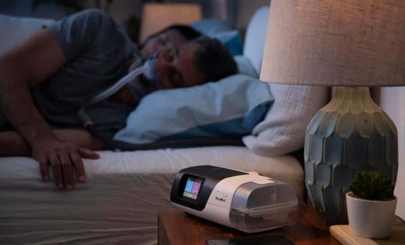CPAP machine on nightstand with man sleeping in background